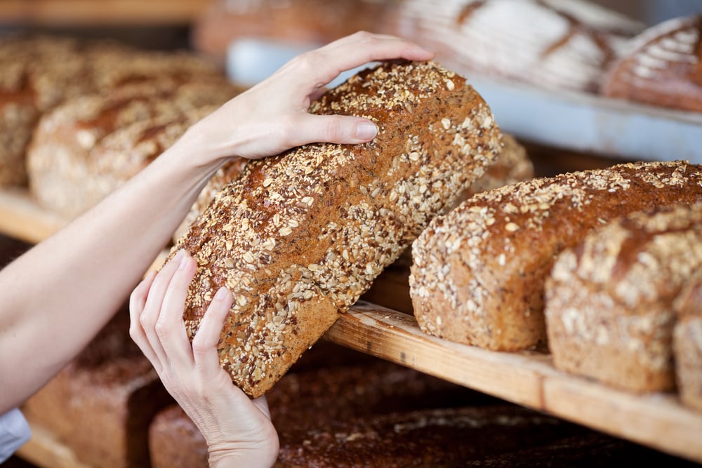 Cropped image of female bakery workers hands removing whole grain bread loaf from shelves